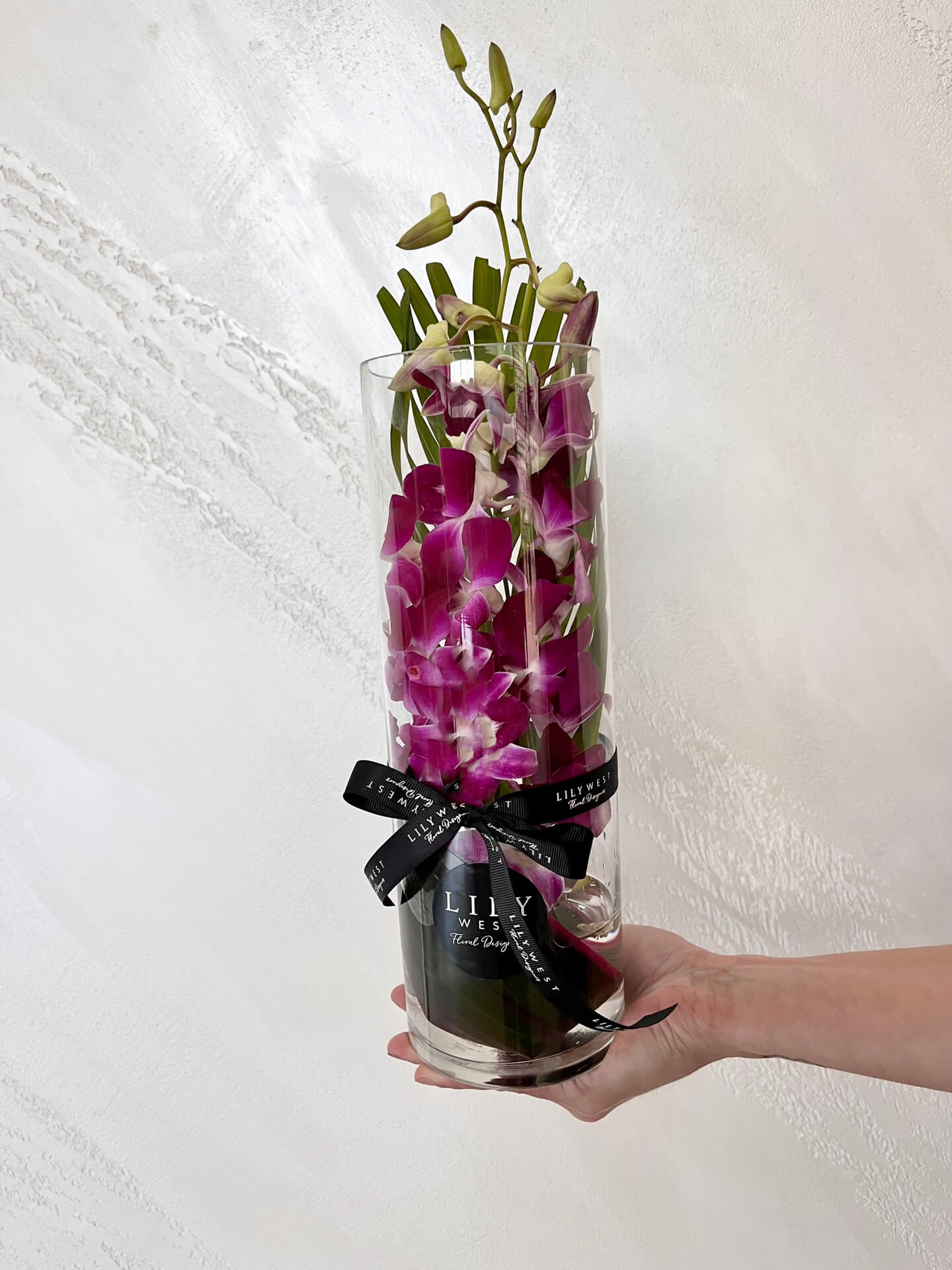 Purple Singapore orchid stems arranged with tropical foliage in a glass vase.