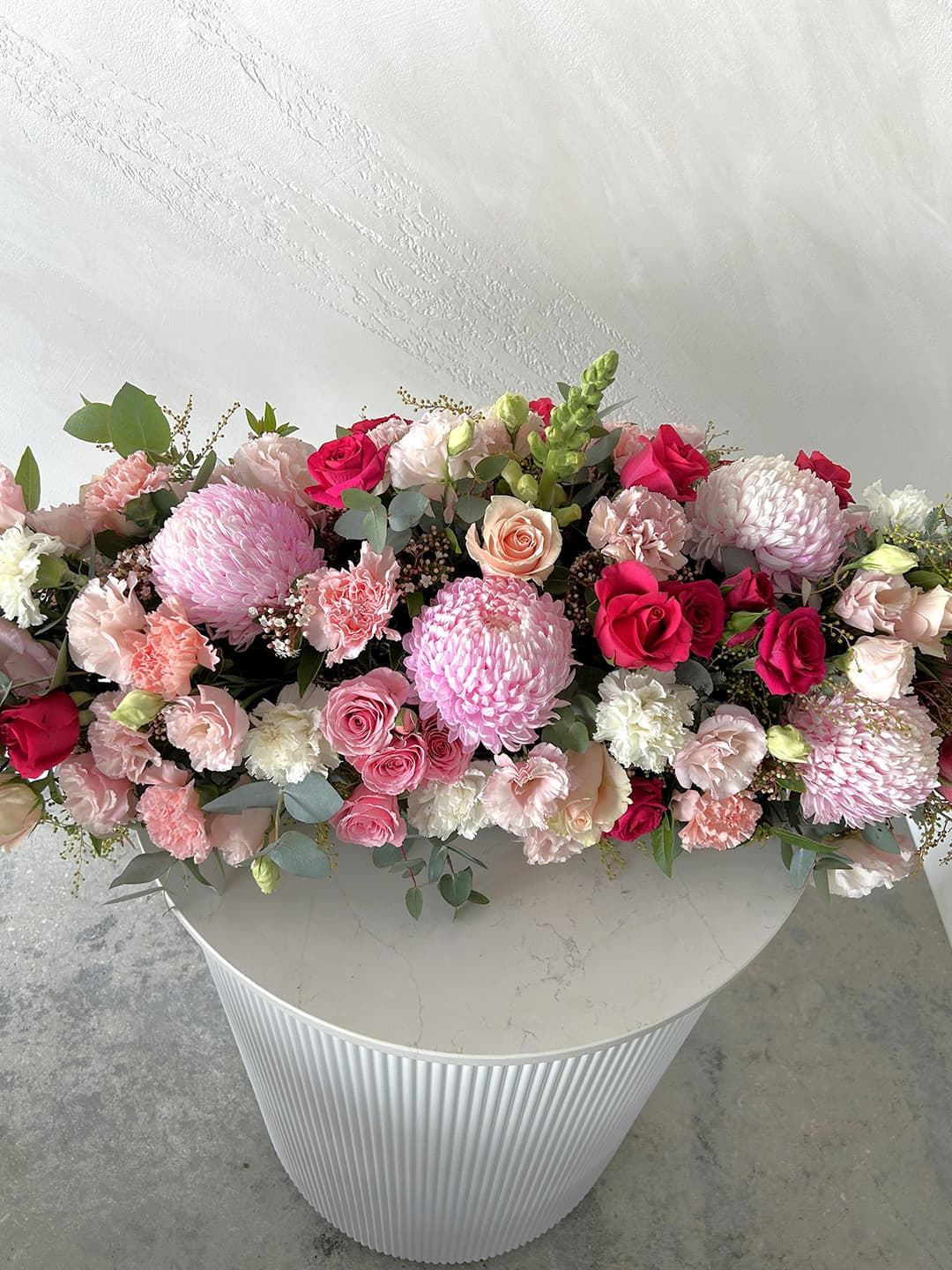Colorful flower arrangement on a white pedestal against a light background