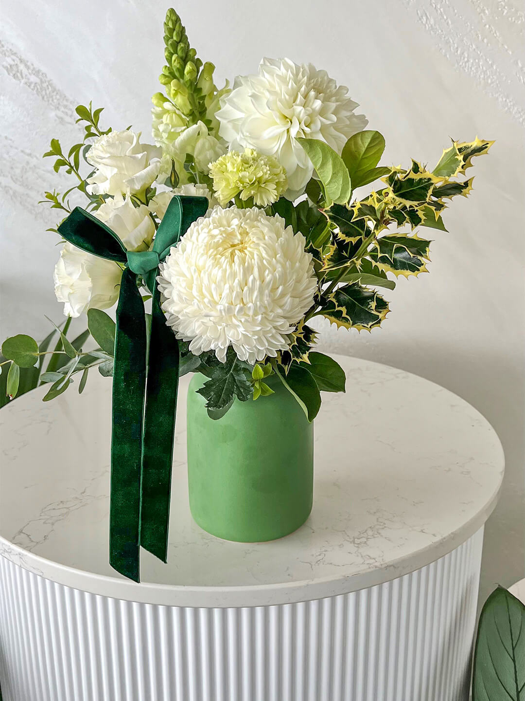 White and green seasonal flowers in a green ceramic vase with ribbon. 