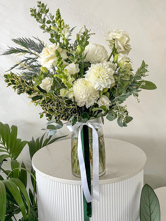 A large vase arrangement with crisp white flowers and seasonal foliage