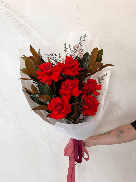 Bouquet of  six premium red roses and foliage wrapped and finished with ribbons.