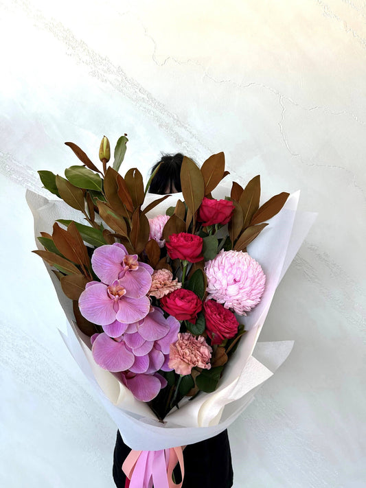 A forward facing bouquet featuring an orchid premium roses mums and carnations with lush foliage