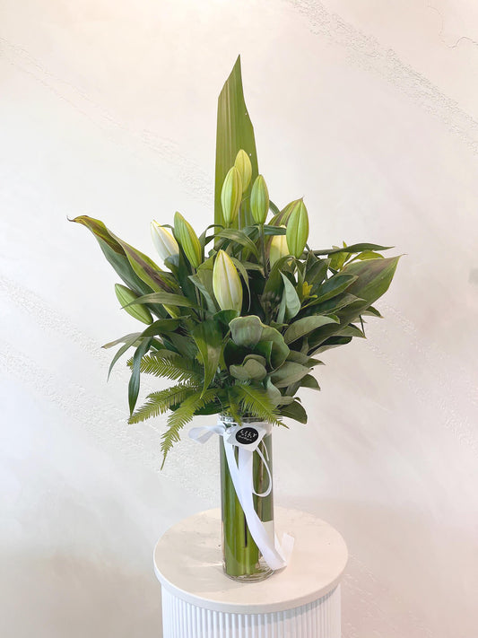 Expertly arranged with green lush foliage, this elegant oriental lily arrangement in a tall clear glass vase exudes a timeless beauty. The pristine white flowers create a stunning centerpiece for any occasion, bringing a touch of sophistication and natural charm to your space.
