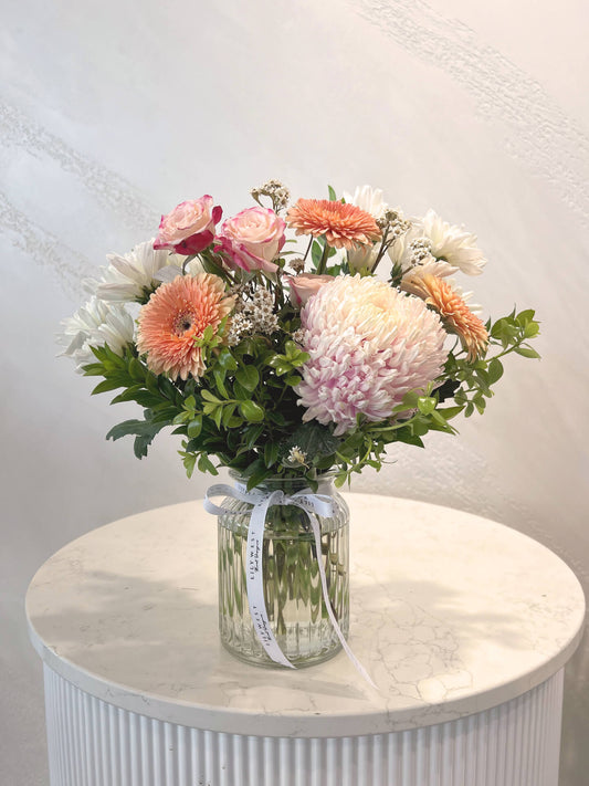 A small posy of seasonal mixed blooms and foliage in a ribbed vase.