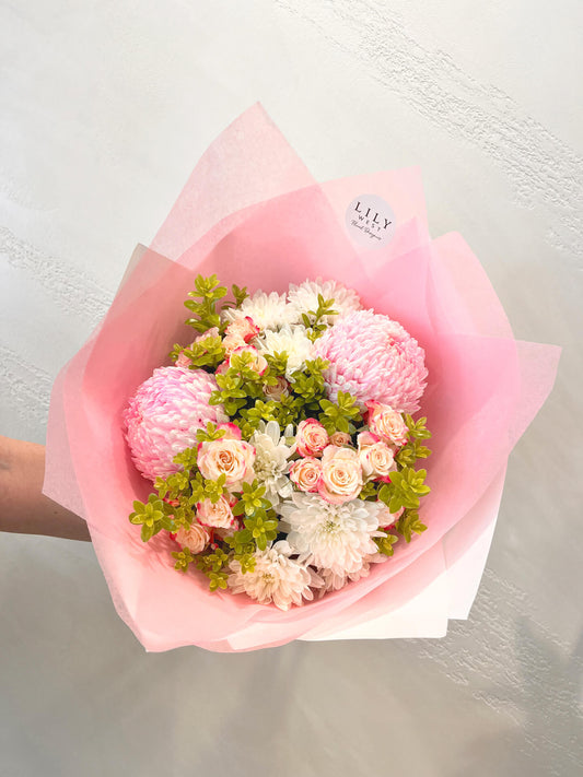 A pretty feminine bouquet with mums, spray roses, daisies and green foliage, wrapped and tied with ribbons.