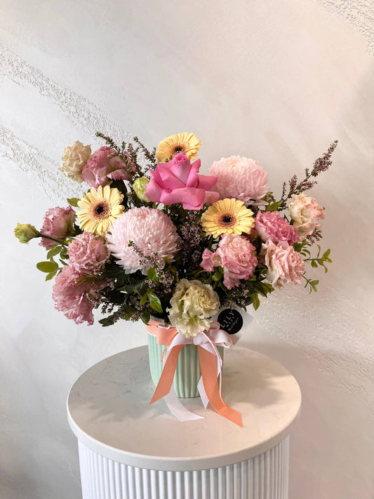 A pretty flower arrangement of mini gerberas, mums, lissianthus made in a pastel ceramic vase. 