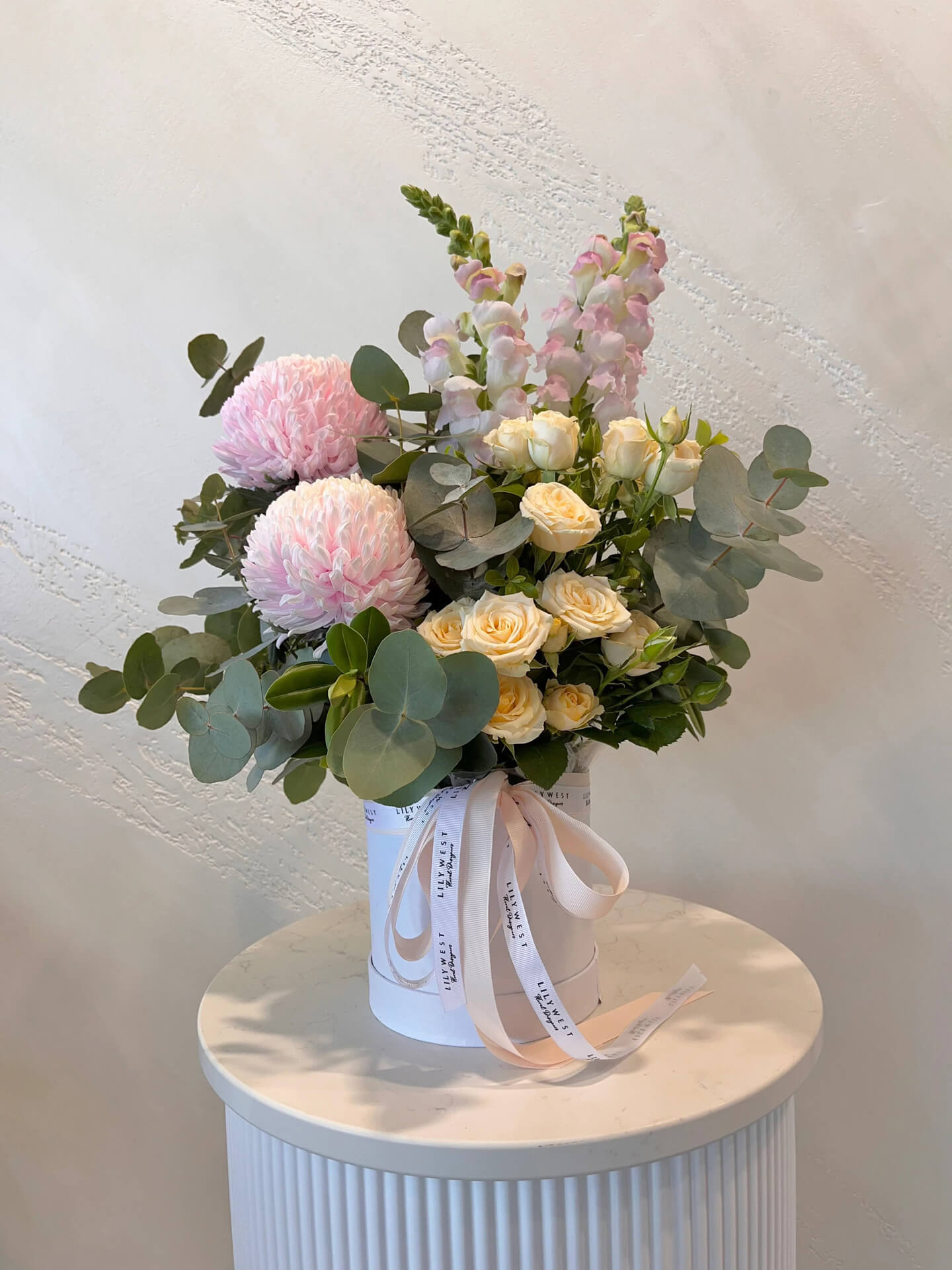 Pastel spray roses snapdragens and mums arranged in a hat box. 